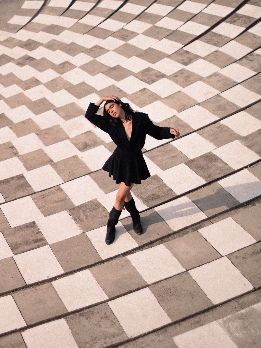 Woman in Black Coat and Black Pants Standing on White and Brown Floor Tiles